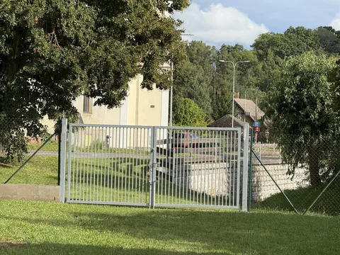 Kovová brána v oplocení u travnatého pozemku