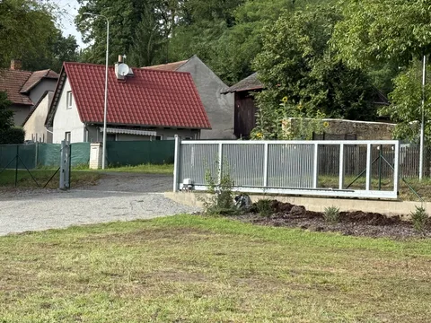 Trávník před kovovým plotem a domem s červenou střechou